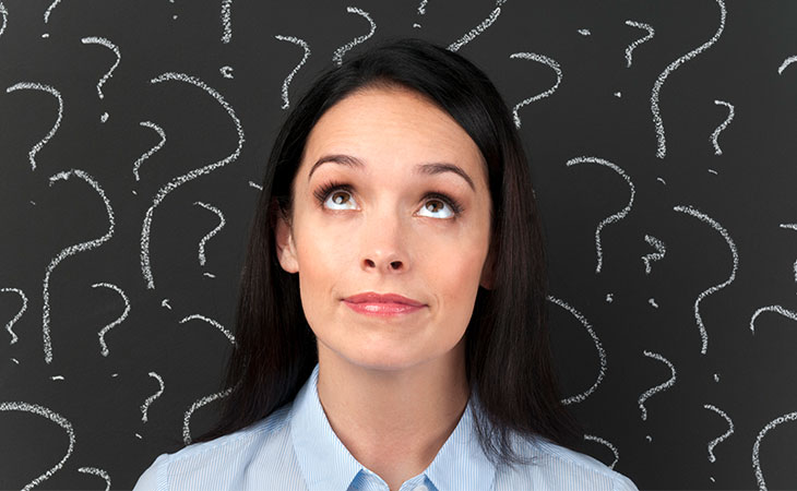 Woman standing in front of a chalkboard background with question marks